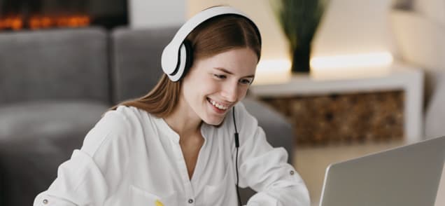 a smiling woman watching a laptop using headphones